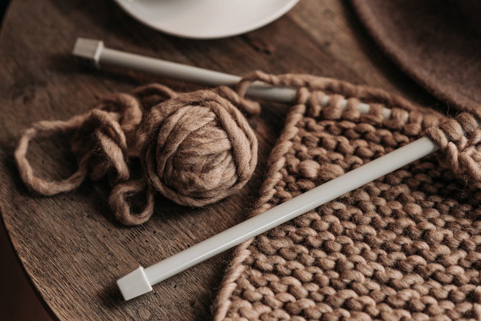 Knitting needles and yarn alongside cross-stitch hoop on wooden table